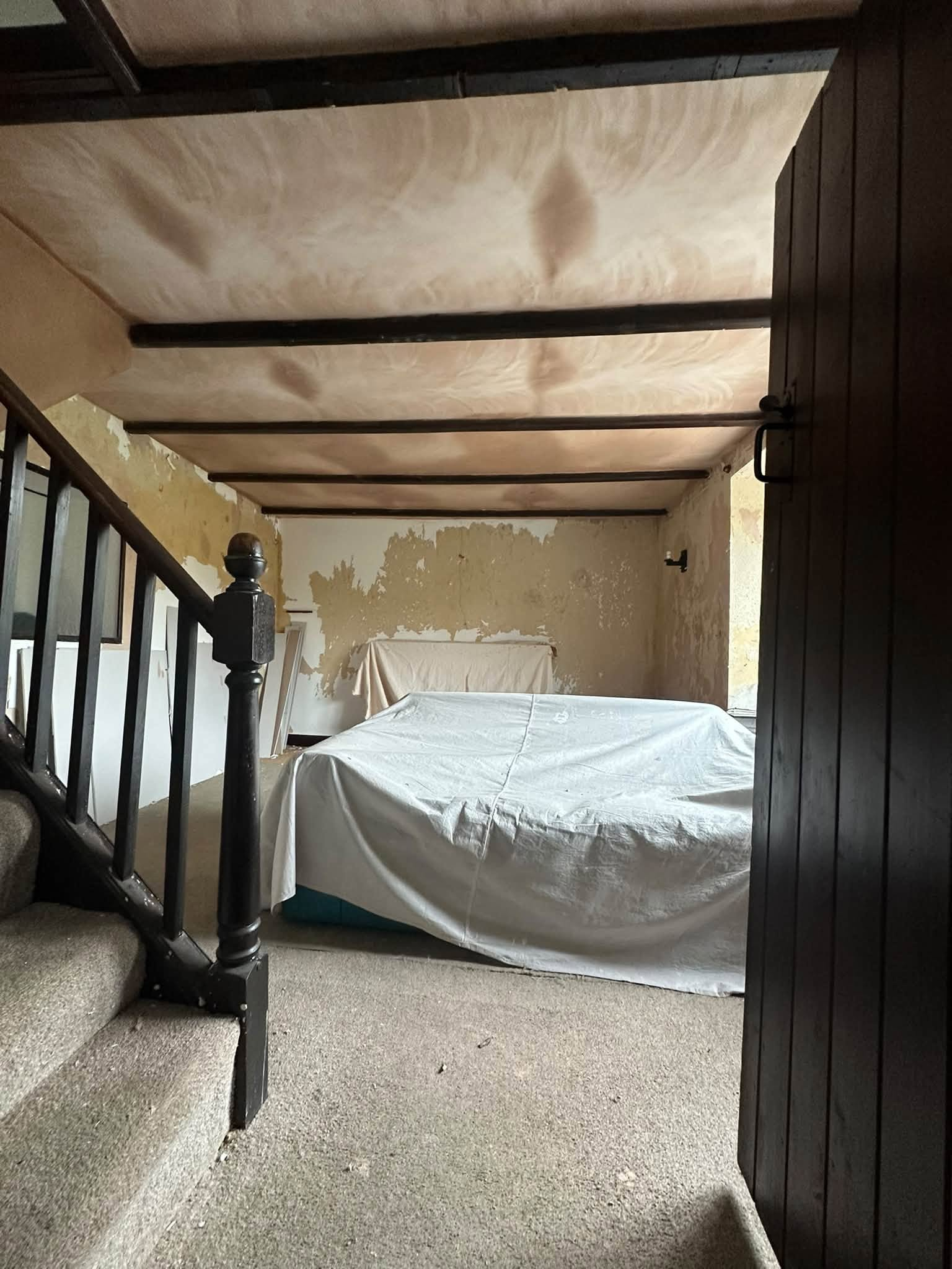 Fresh plaster between exposed beams above covered furniture beside a staircase