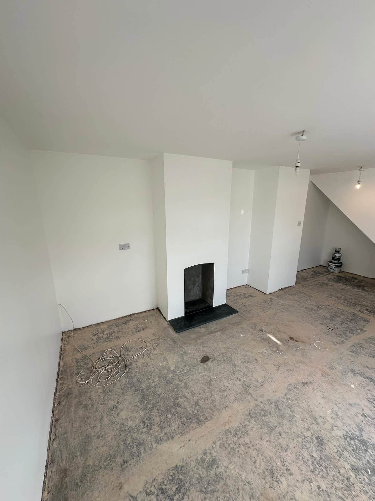 White walls and ceiling surrounding a fireplace, with bare flooring during renovation