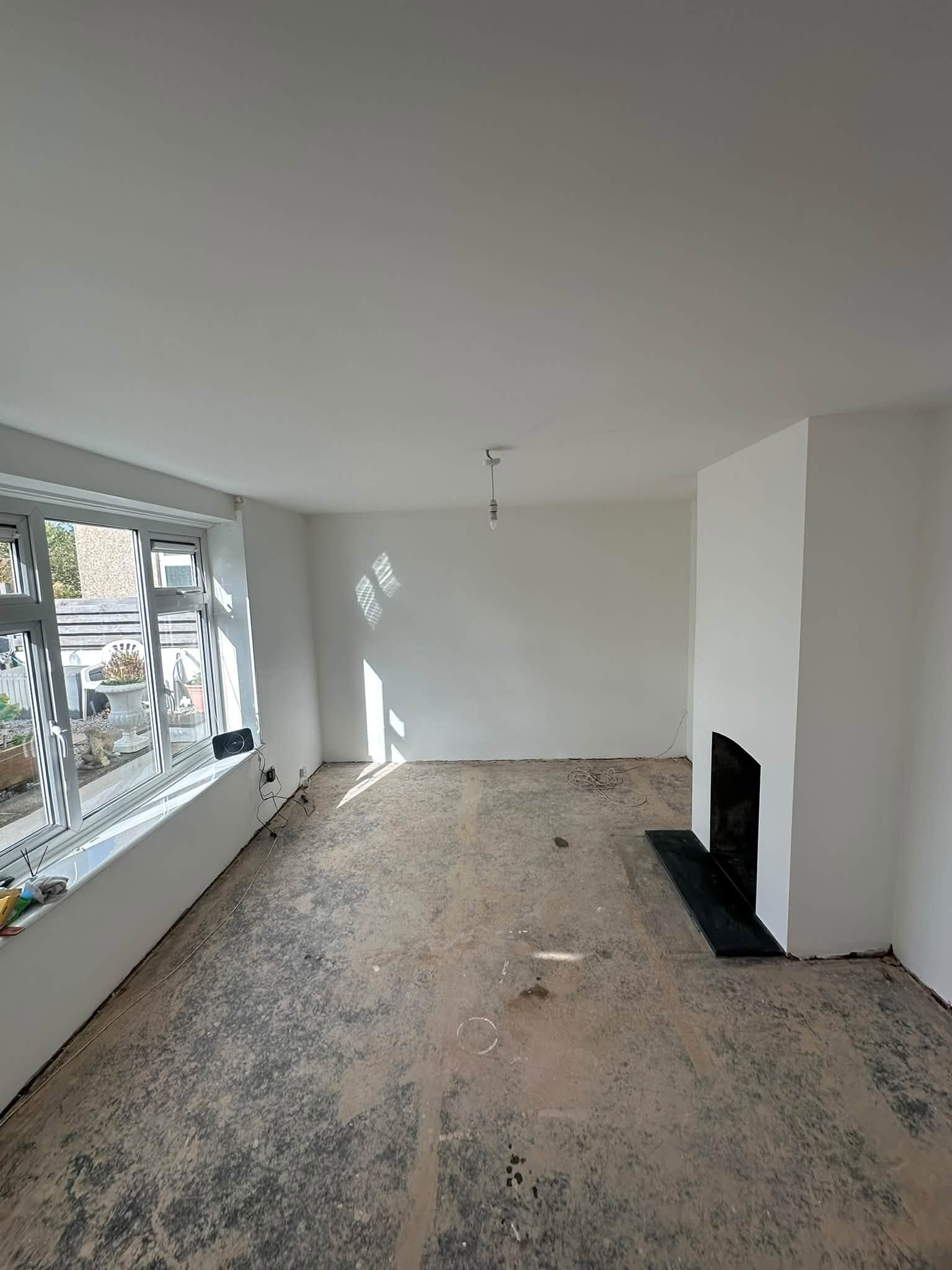 White walls and ceiling beside large windows and a fireplace, with bare flooring