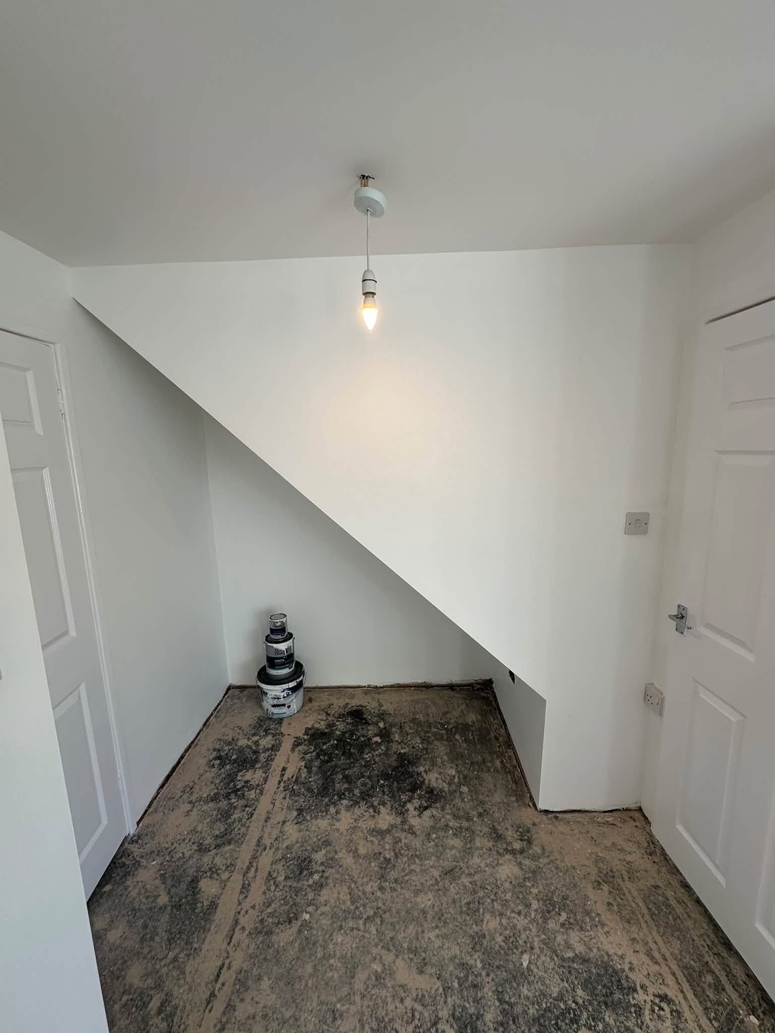 White sloping wall between two doors, with paint tins and bare flooring