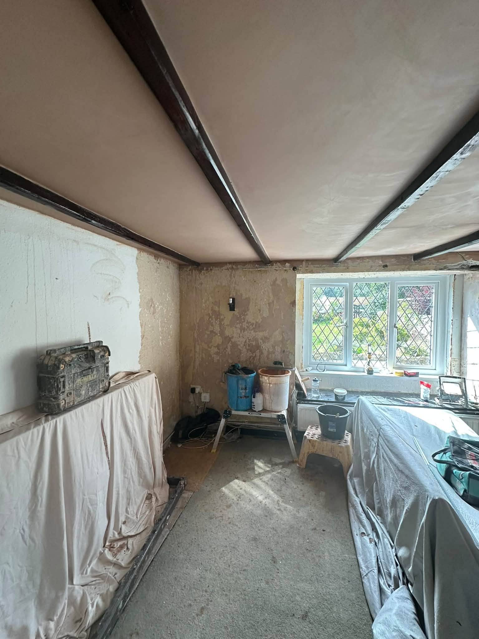 Fresh plaster between dark ceiling beams, with covered furniture and stripped walls
