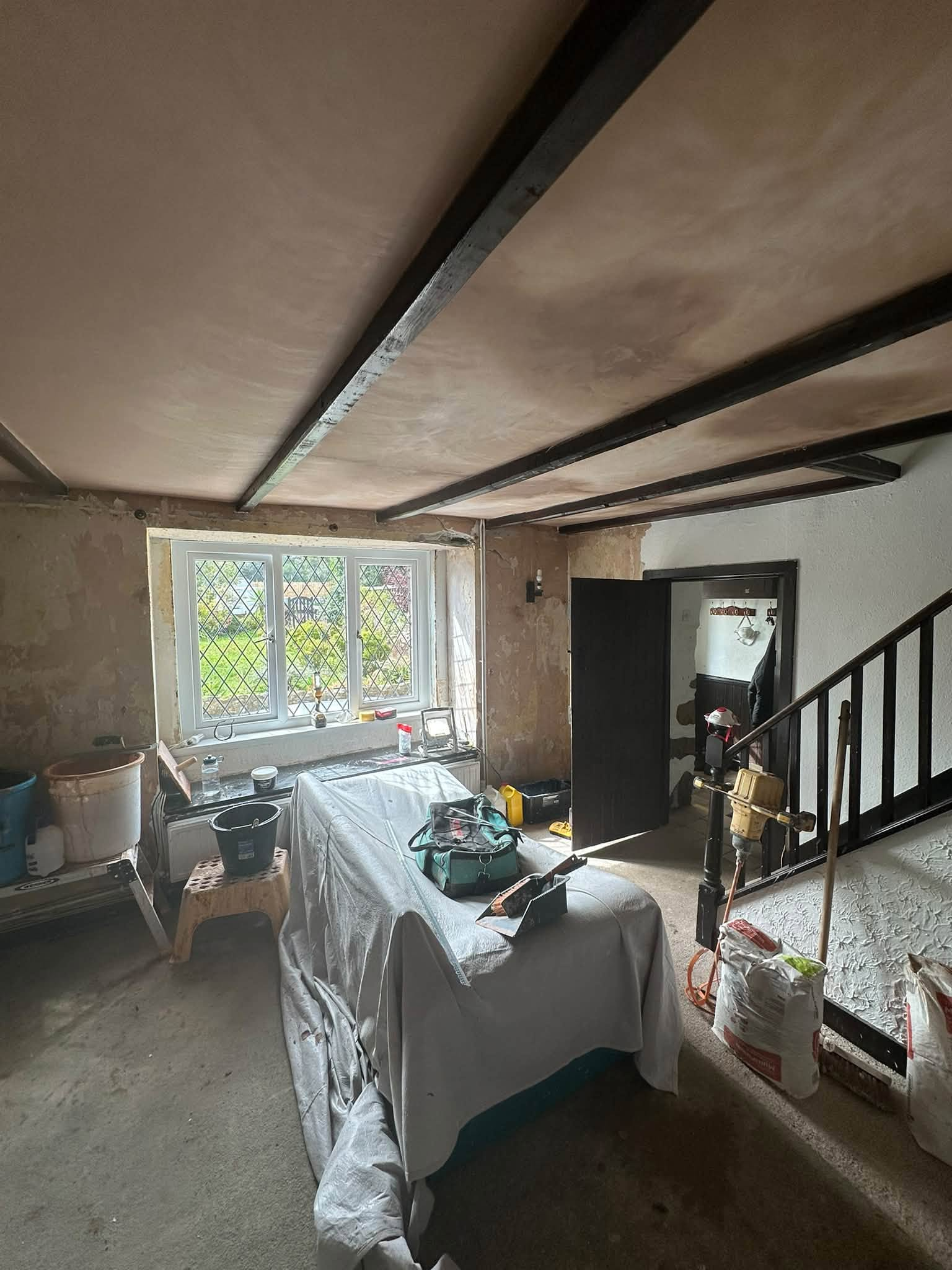 Freshly plastered ceiling around dark beams beside a stairwell during renovation